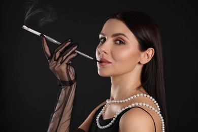 Woman using long cigarette holder for smoking on black background