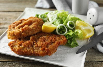 Photo of Tasty schnitzels served with lemon and salad on wooden table, closeup