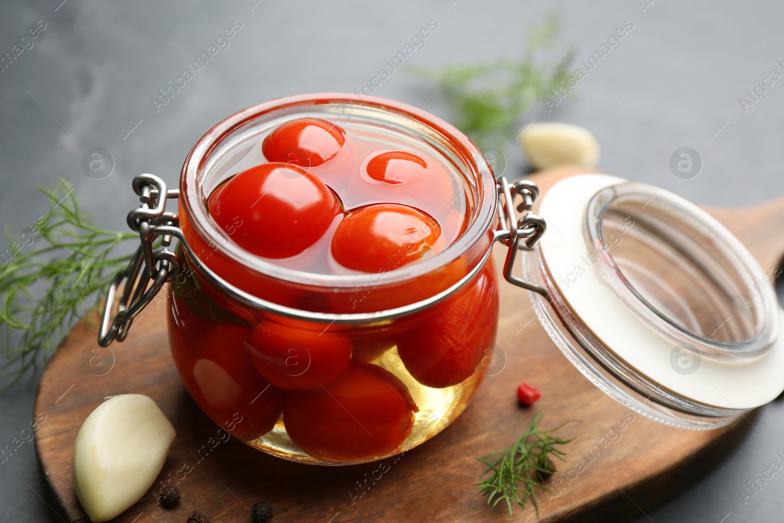 Photo of Glass jar of pickled cherry tomatoes on wooden board, closeup