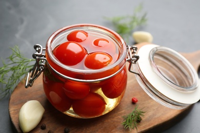 Glass jar of pickled cherry tomatoes on wooden board, closeup