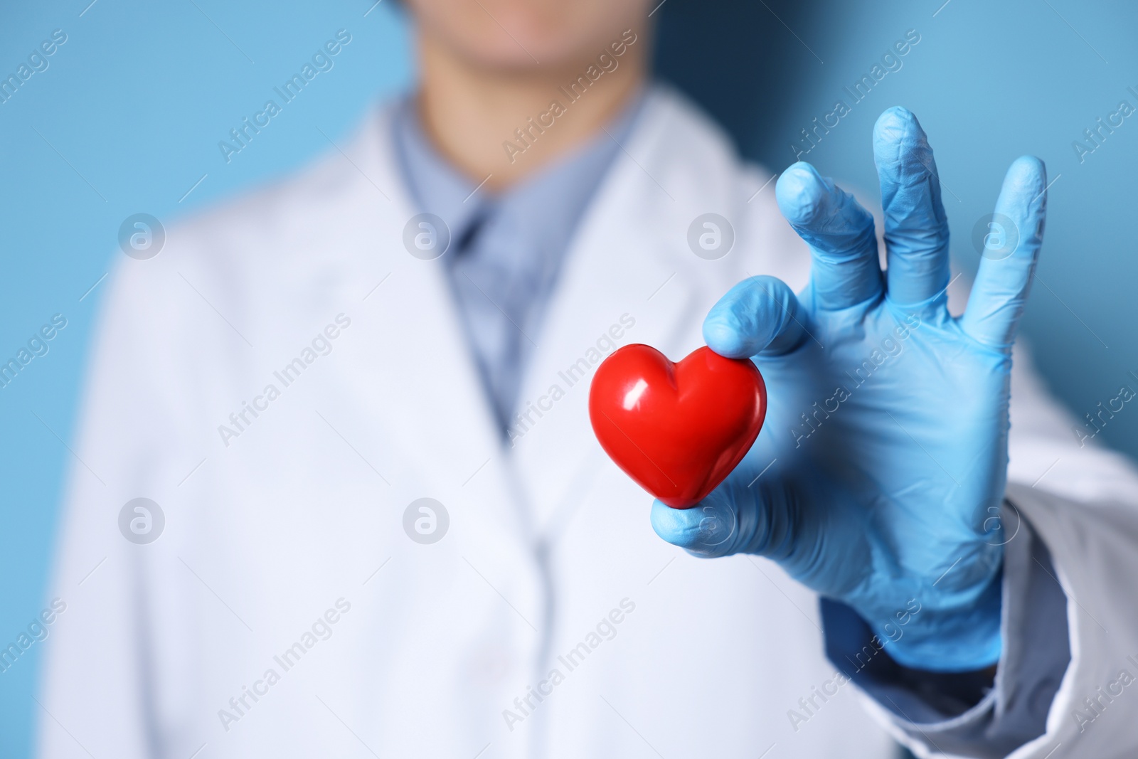 Photo of Doctor wearing medical gloves holding decorative heart on light blue background, closeup