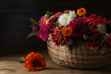 Beautiful wild flowers and leaves in wicker basket on wooden table, closeup