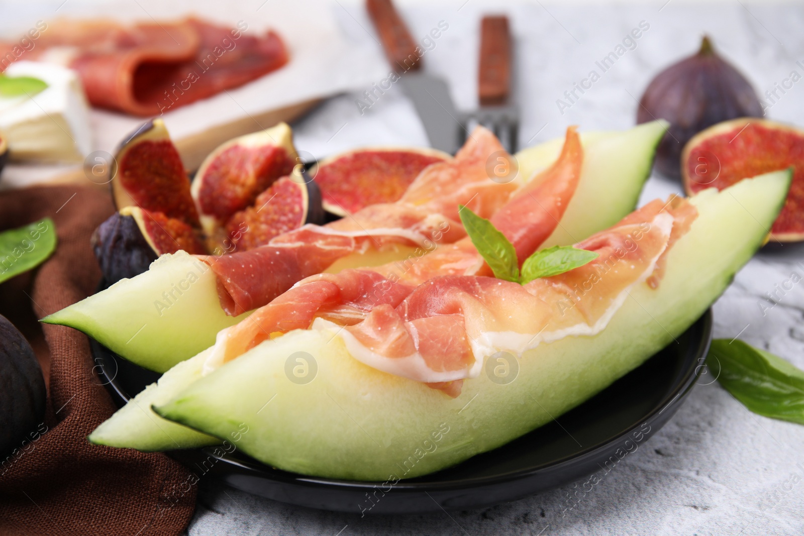 Photo of Tasty melon, jamon and figs served on white textured table, closeup