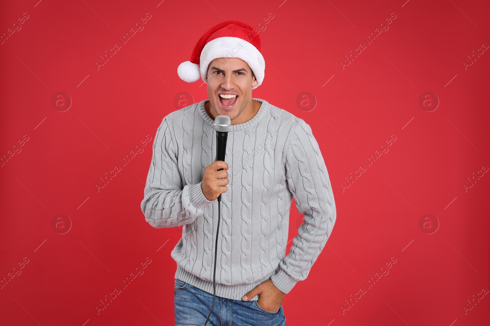 Photo of Happy man in Santa Claus hat singing with microphone on red background. Christmas music