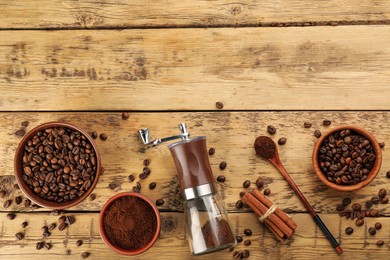 Modern manual coffee grinder with beans, powder and cinnamon on wooden table, flat lay. Space for text
