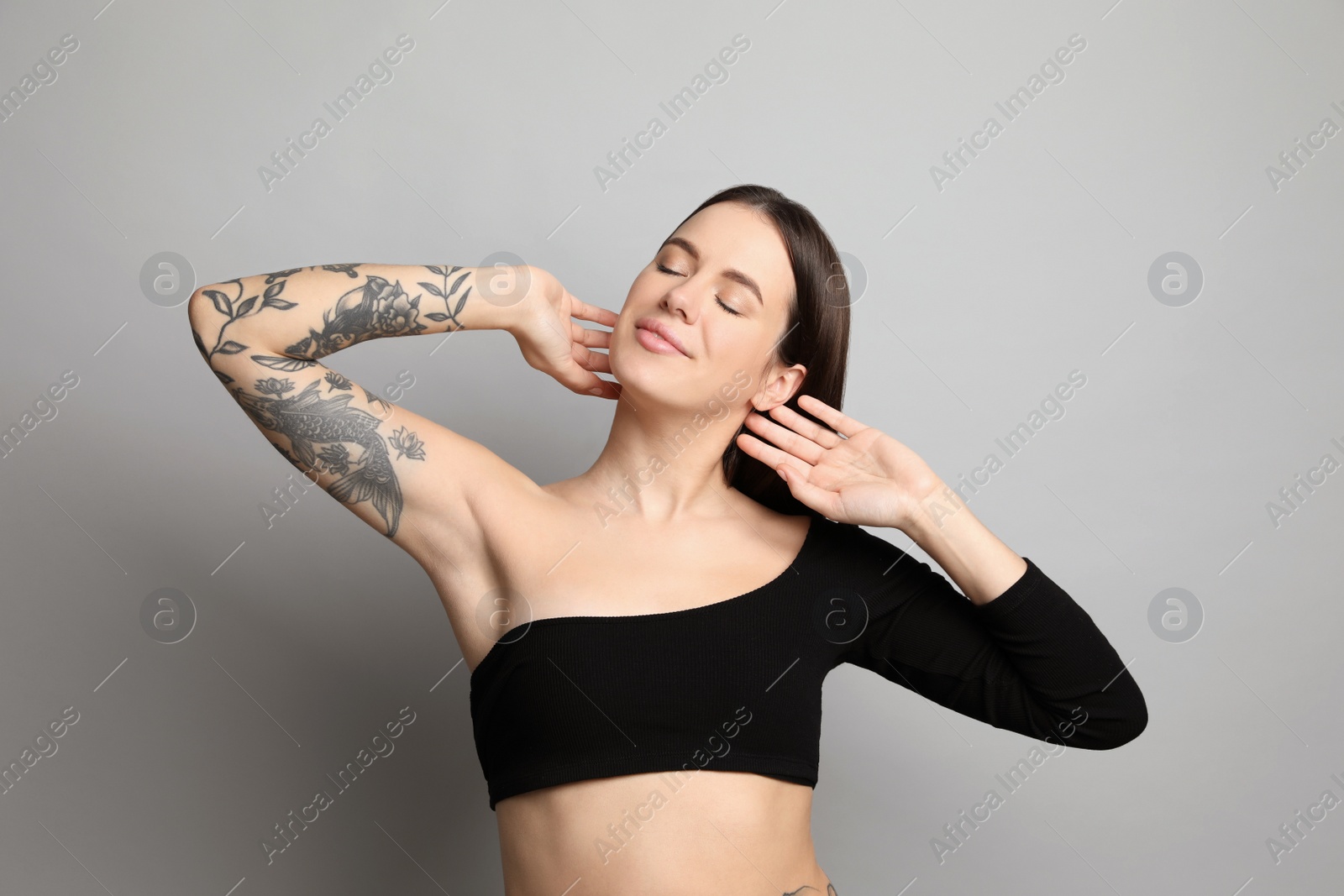 Photo of Beautiful woman with tattoos on arm against grey background