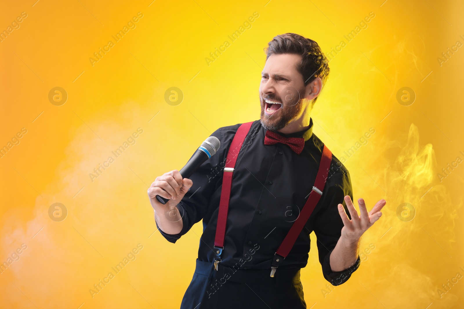 Photo of Emotional man with microphone singing on yellow background. Space for text