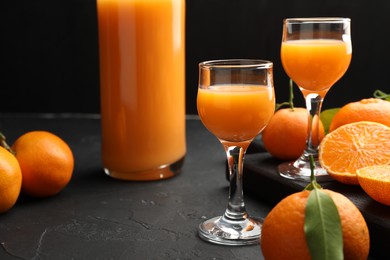 Photo of Tasty tangerine liqueur and fresh fruits on black textured table