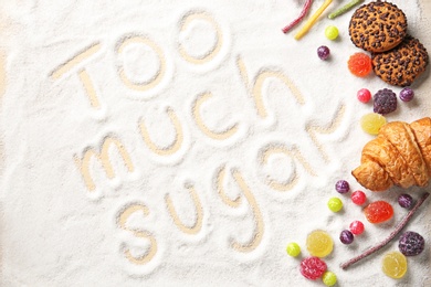 Photo of Composition with sweets and phrase TOO MUCH SUGAR written on sugar sand