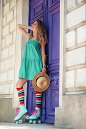 Photo of Happy girl with retro roller skates standing near violet door