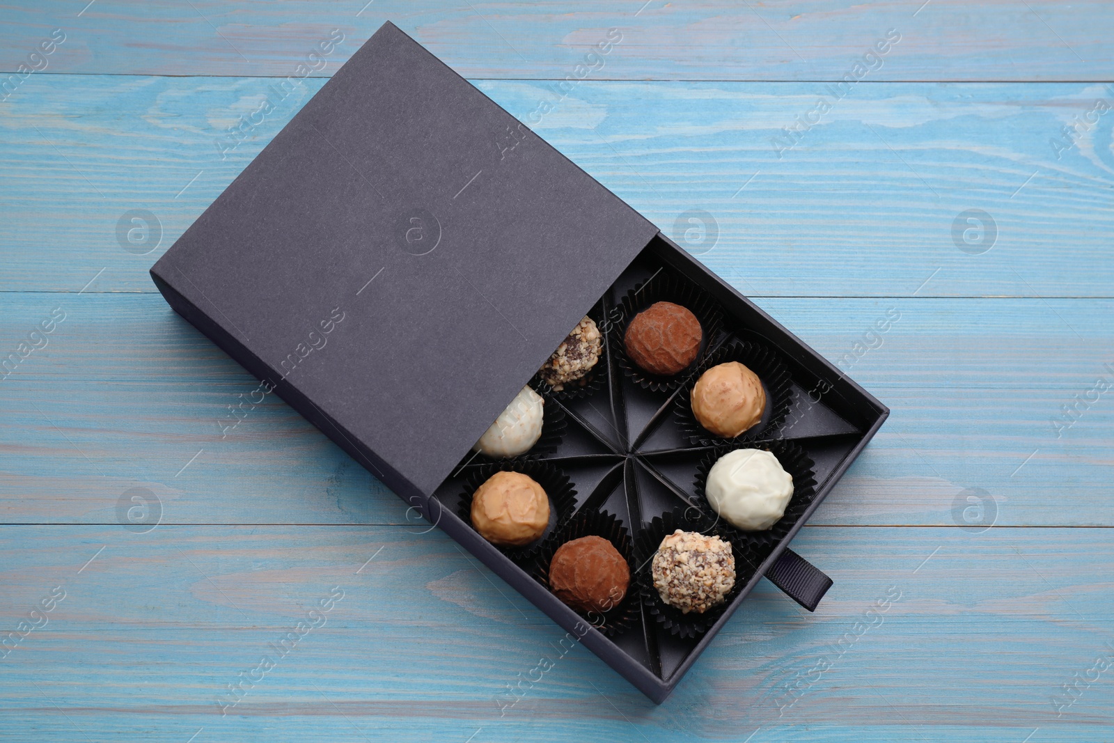 Photo of Box of tasty chocolate candies on light blue wooden table, top view