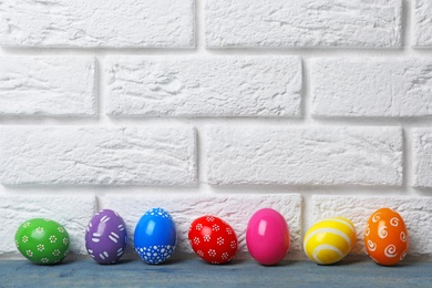 Photo of Decorated Easter eggs on table near brick wall. Space for text