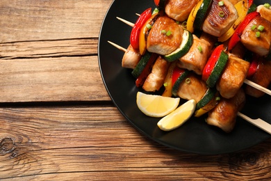 Delicious chicken shish kebabs with vegetables and lemon on wooden table, top view. Space for text