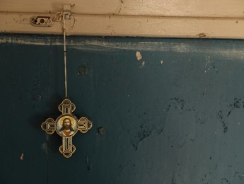 Cross with icon hanging on blue wall indoors, space for text