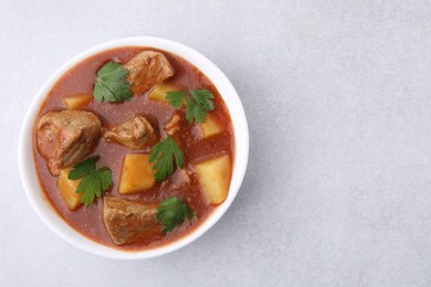 Delicious goulash in bowl on light grey table, top view. Space for text