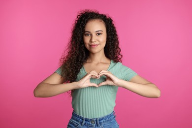 Photo of Happy young African-American woman making heart with hands on pink background