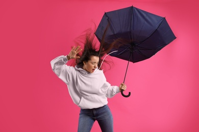 Photo of Emotional woman with umbrella caught in gust of wind on pink background