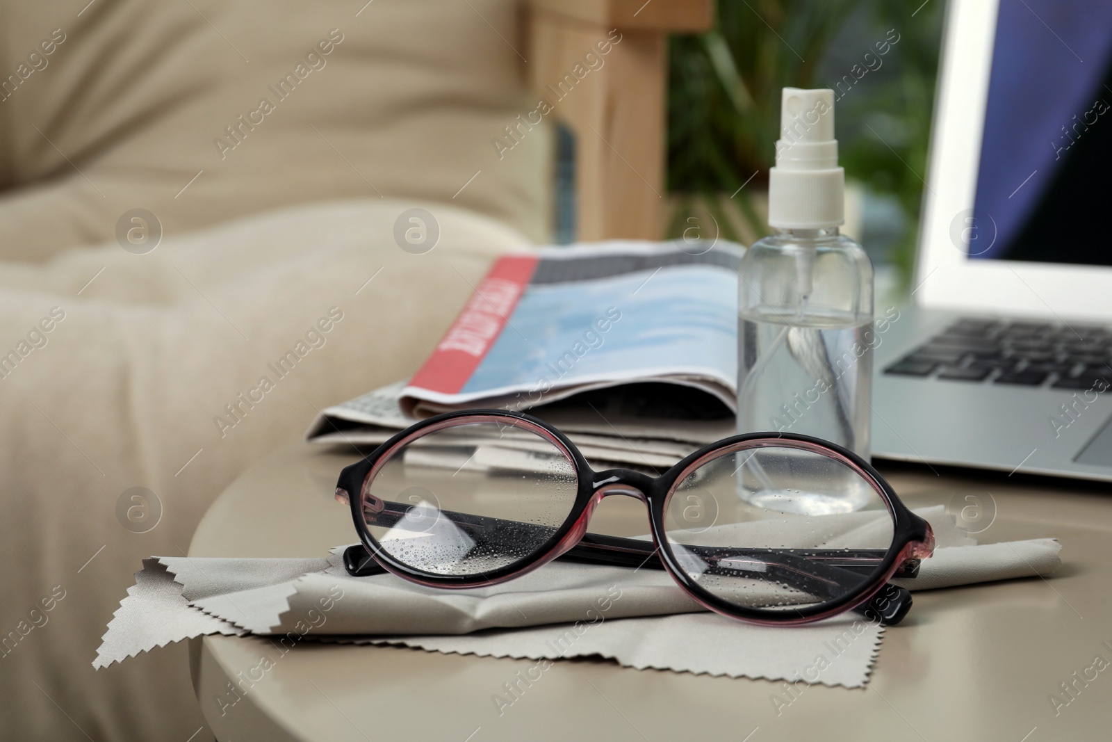 Photo of Glasses, microfiber cloth and spray bottle on table indoors