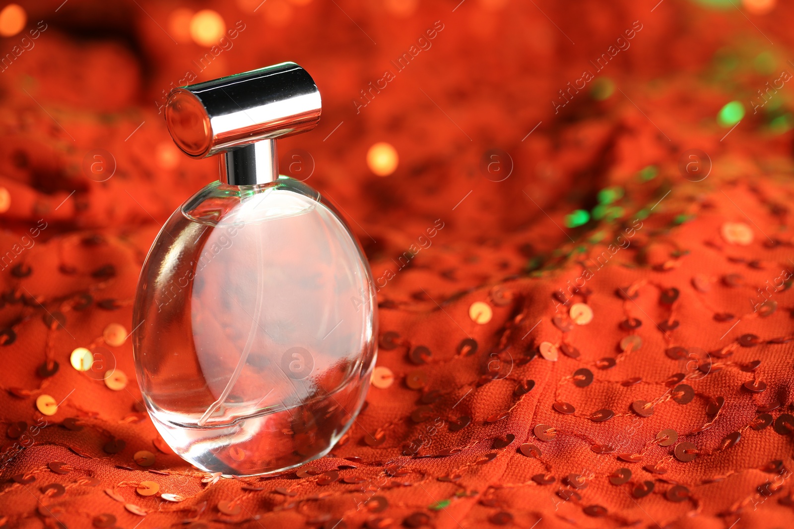 Photo of Luxury perfume in bottle on red fabric with sequins, closeup