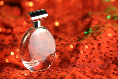 Photo of Luxury perfume in bottle on red fabric with sequins, closeup