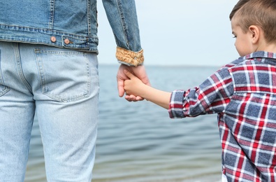 Photo of Cute little child holding hands with his father near river. Family time
