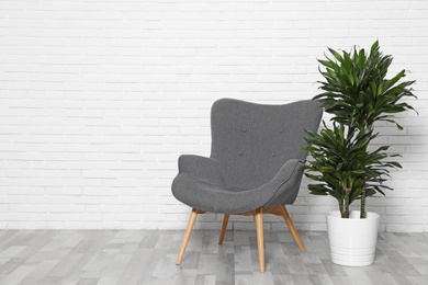 Dracaena and chair at white brick wall, space for text. Plants in trendy home interior design