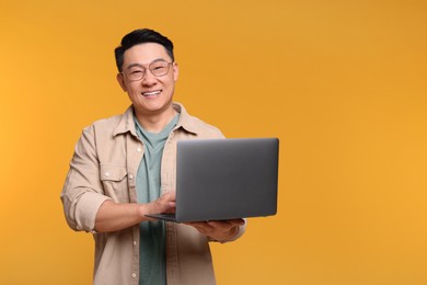 Photo of Happy man with laptop on yellow background, space for text