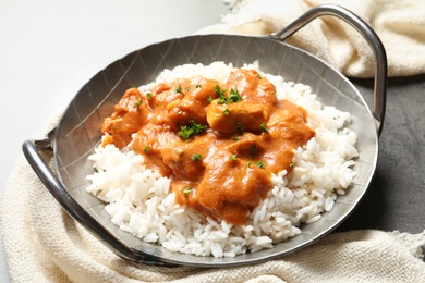 Photo of Delicious butter chicken with rice in dish and napkin on table