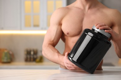 Photo of Young man with jar of protein powder at white marble table in kitchen, closeup. Space for text