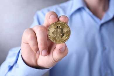 Photo of Man holding golden bitcoin on color background, closeup