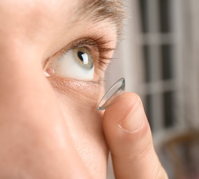 Photo of Young man putting contact lens into his eye, closeup