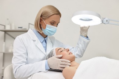 Dermatologist examining patient`s face under lamp in clinic