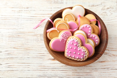 Photo of Bowl with decorated heart shaped cookies on wooden table