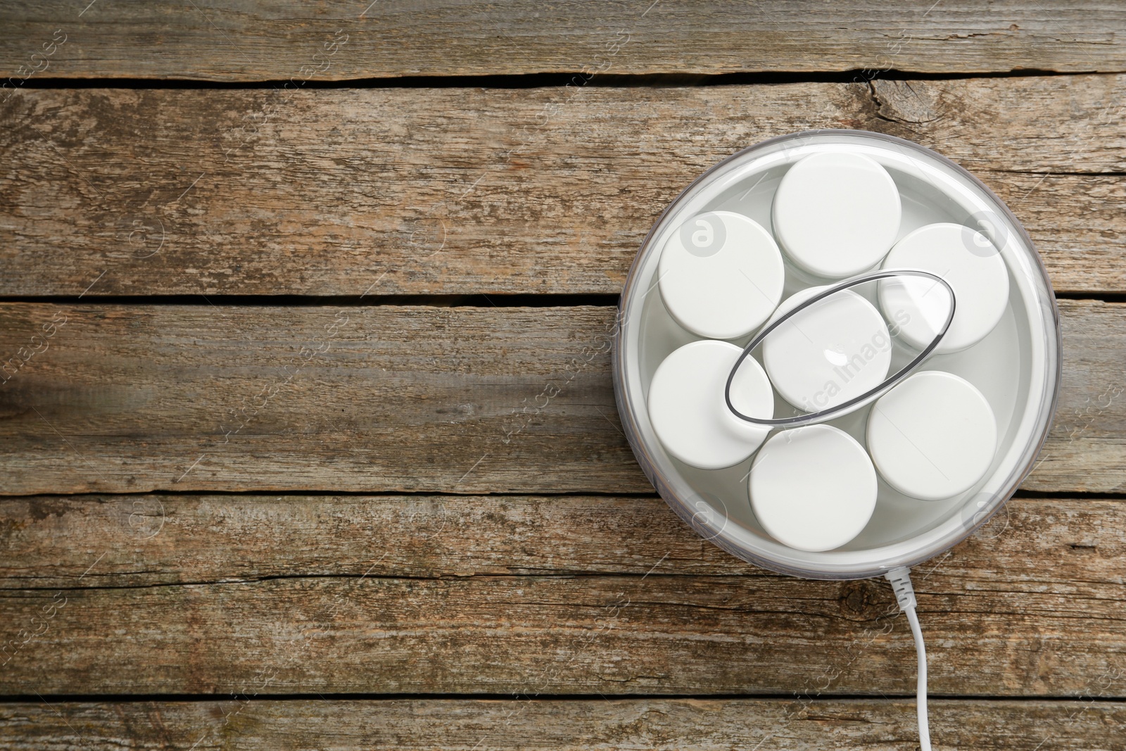 Photo of Modern yogurt maker with jars on wooden table, top view. Space for text