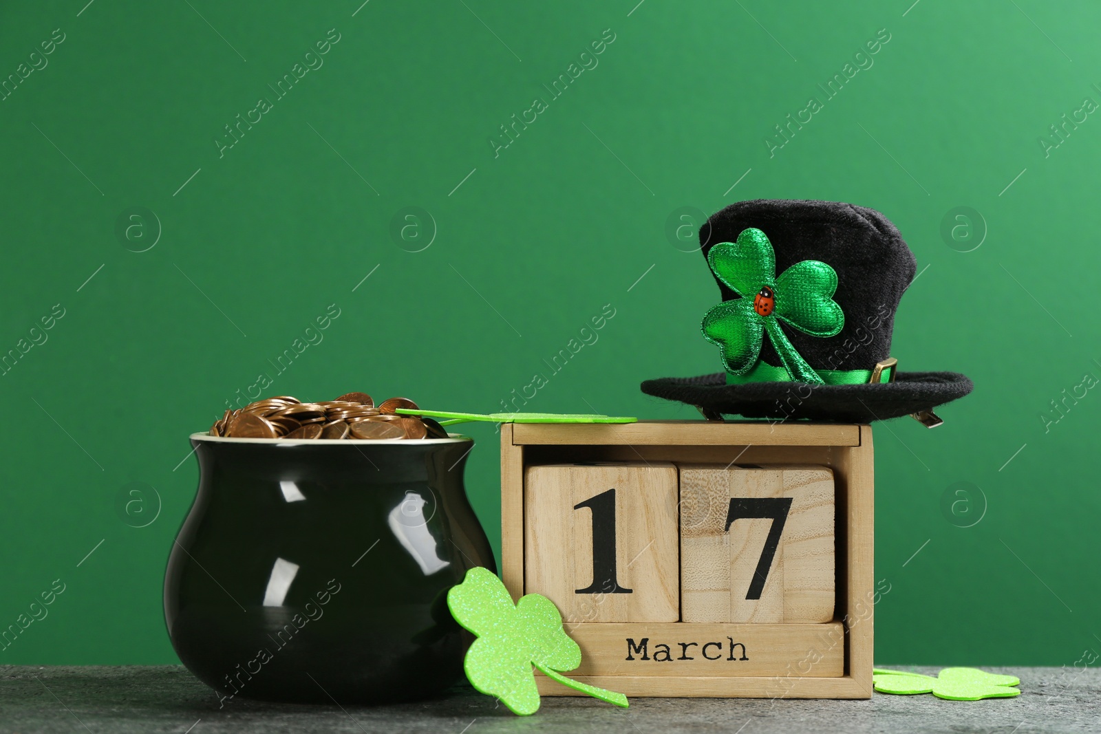 Photo of Composition pot of gold coins and wooden block calendar on grey stone table against green background. St. Patrick's Day celebration