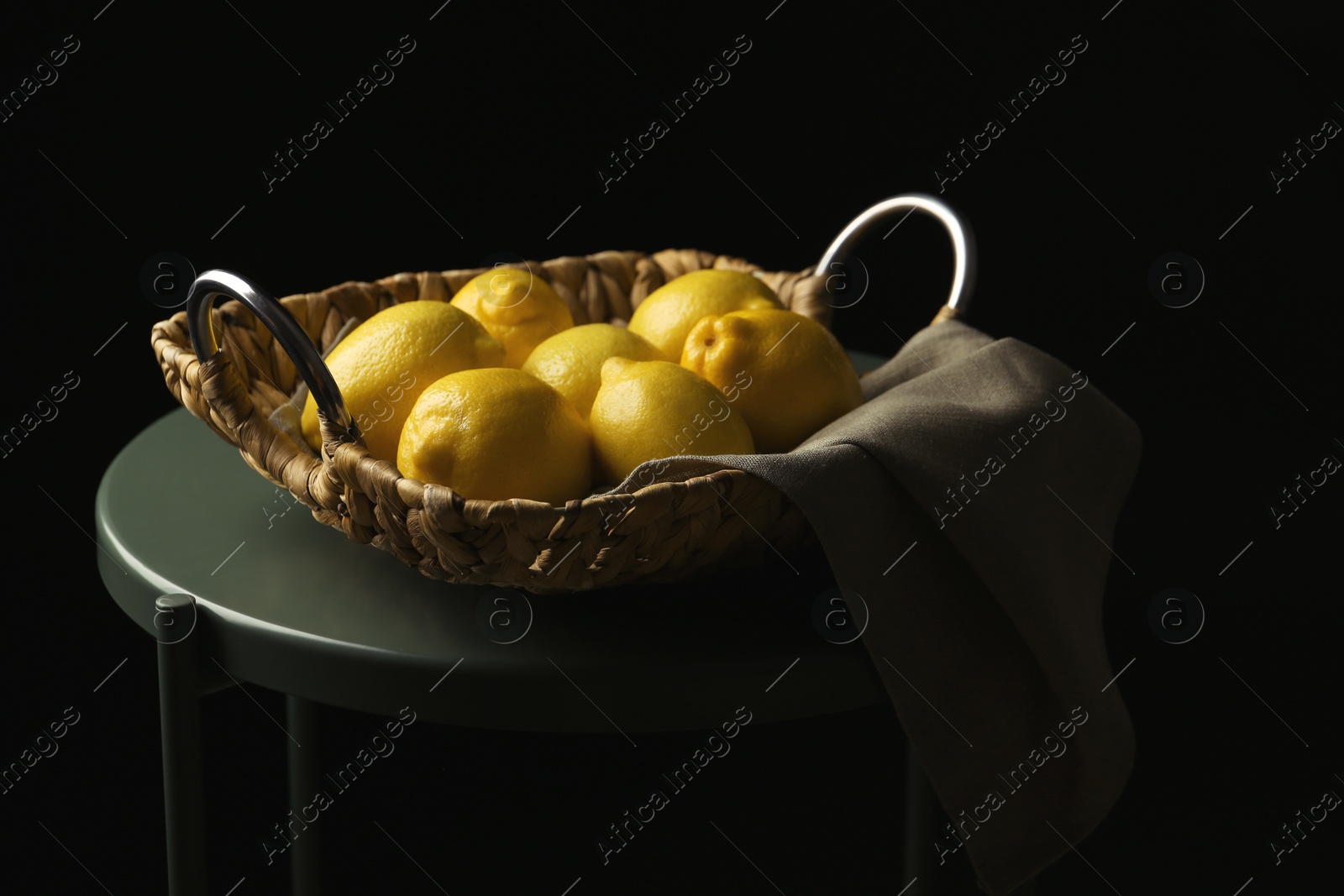 Photo of Basket with whole lemons on small table against dark background
