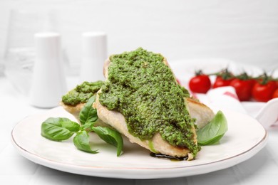 Delicious chicken breasts with pesto sauce and basil on white tiled table