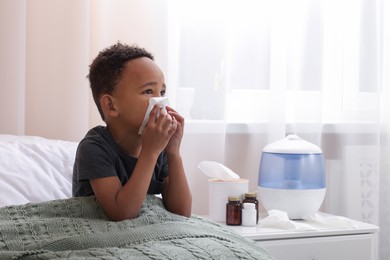 Photo of African-American boy with tissue blowing nose in bed indoors, space for text. Cold symptoms