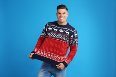 Photo of Happy man showing his Christmas sweater on blue background