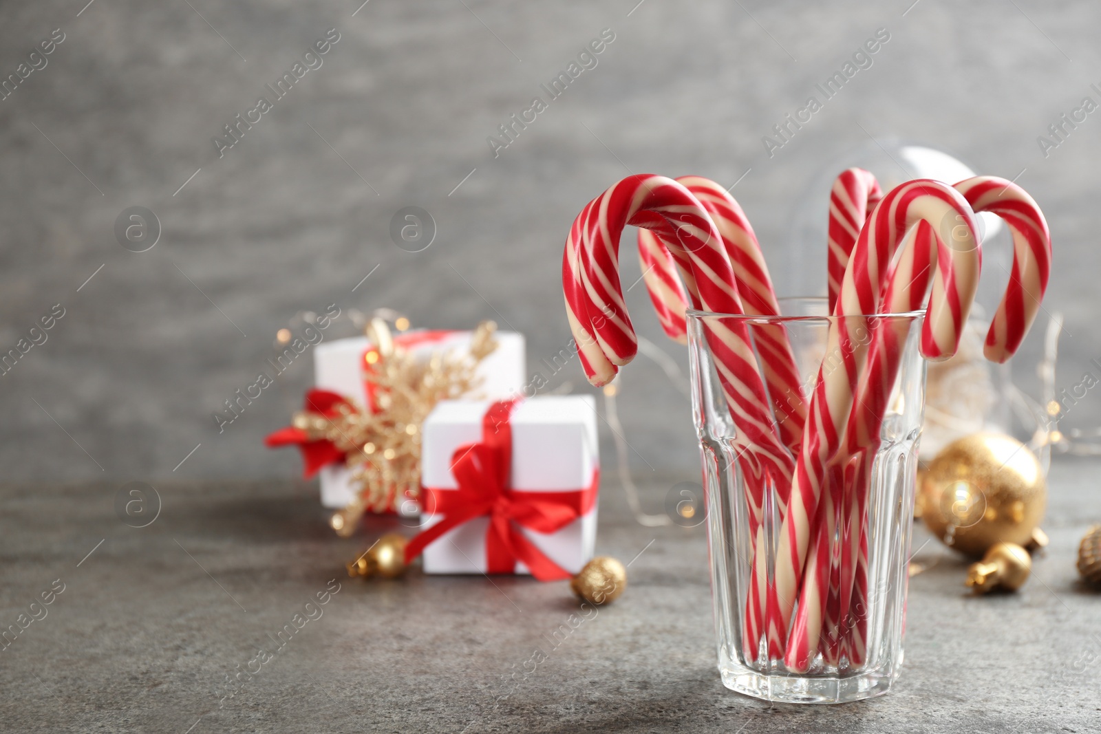 Photo of Christmas candy canes in glass on grey table, space for text