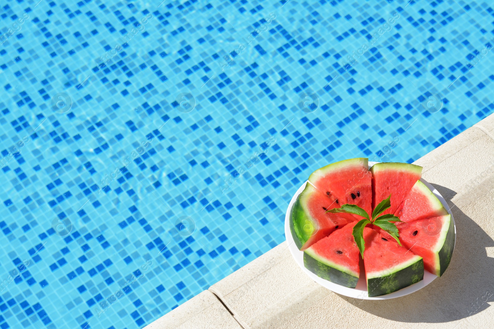 Photo of Slices of watermelon on white plate near swimming pool outdoors. Space for text