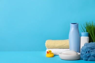 Photo of Baby cosmetic products, bath duck, sponge and towels on light blue background. Space for text