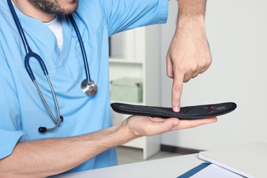 Photo of Male orthopedist showing insole in hospital, closeup