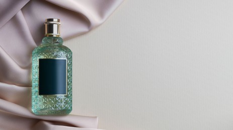 Bottle of luxurious perfume and beige silk fabric on light background, top view. Space for text