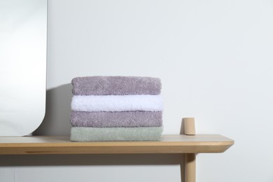 Photo of Stacked terry towels on wooden shelf near white wall