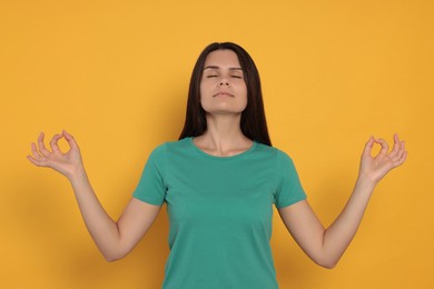 Photo of Young woman meditating on orange background. Zen concept