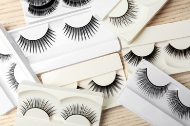 Photo of Different types of false eyelashes in packs on wooden background