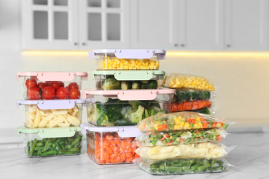 Plastic bags and containers with different frozen vegetables on white marble table in kitchen