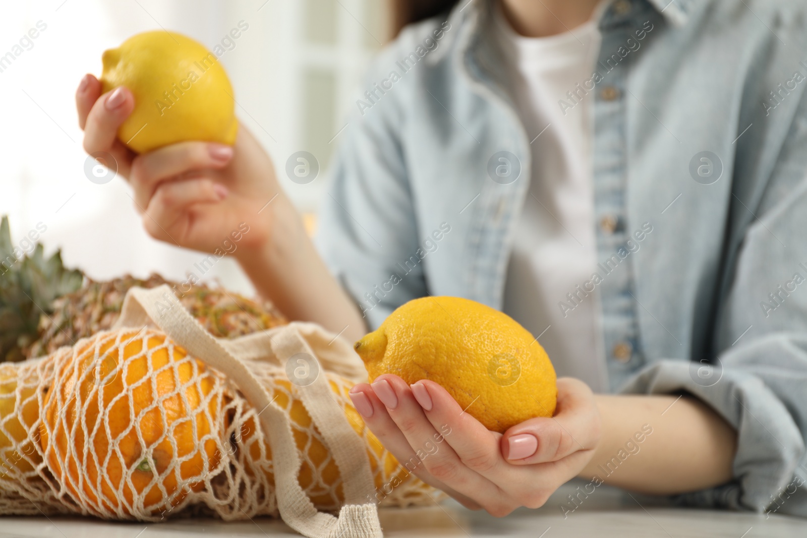 Photo of Woman with lemons and string bag of fresh fruits at light table, closeup