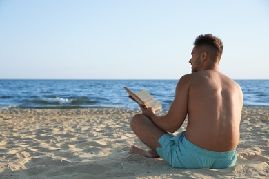 Photo of Young man reading book on sandy beach near sea